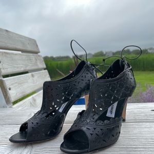 Black patent open toe mules featuring two structured leather lacing detail.